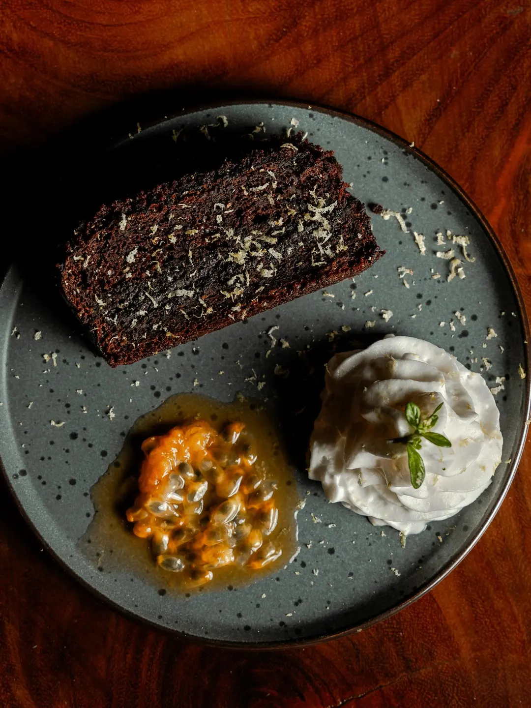Torta de chocolate con ralladura de limón, maracuyá y crema sobre un plato gris.