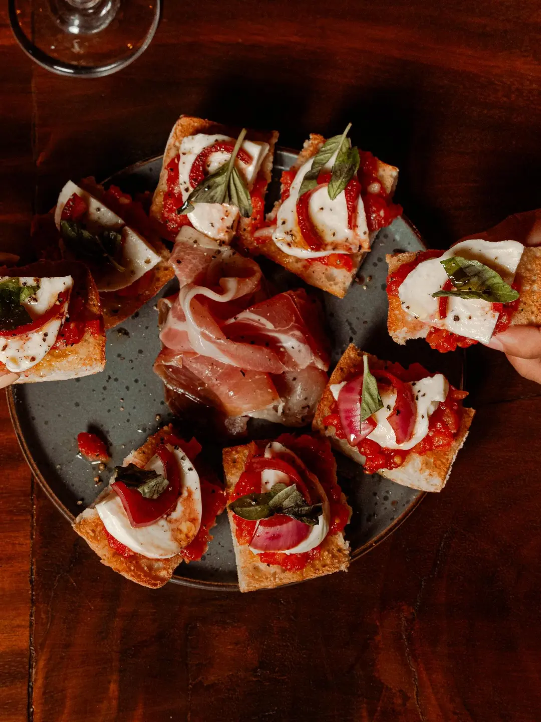 Tostadas con tomate, mozzarella, albahaca y cebolla morada, con jamón en el centro del plato.