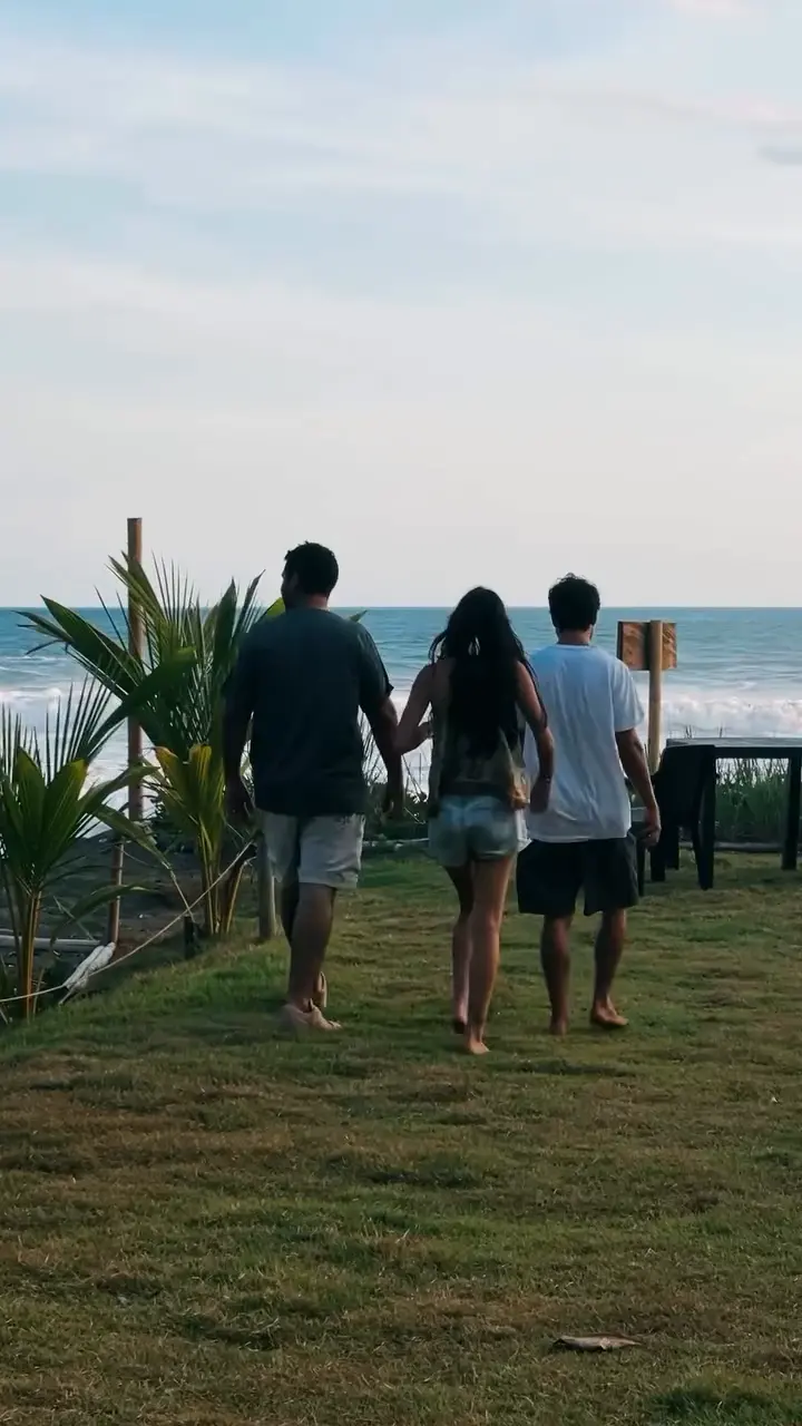 Tres personas, vistas de espaldas, caminando por el césped hacia la playa.